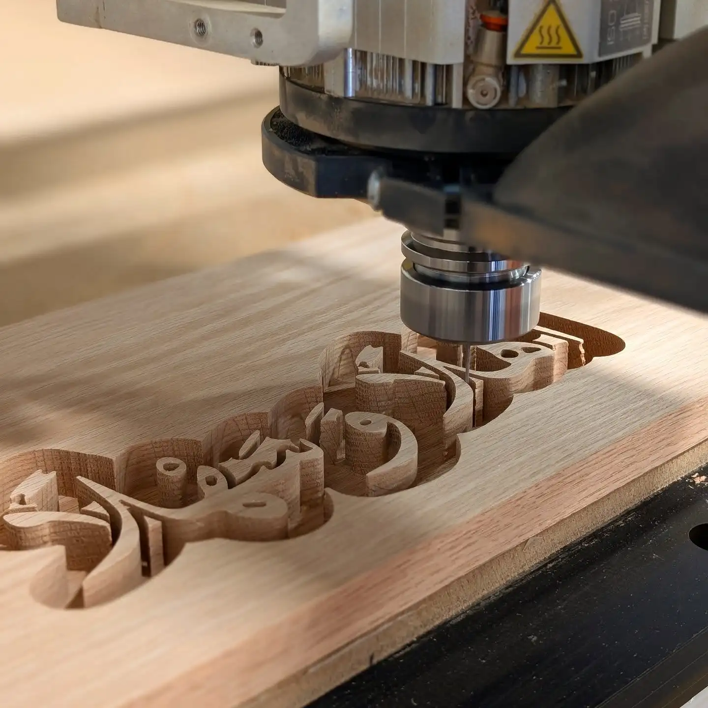 CNC router cutting raised lettering from a solid oak board
